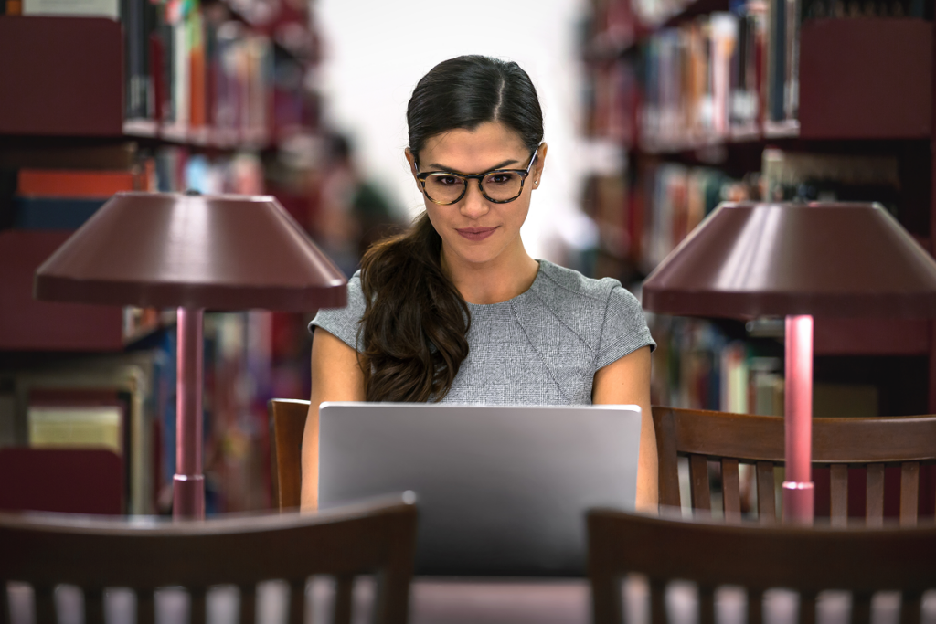 Estudante da pós em direito do consumido estudando no computador em biblioteca.