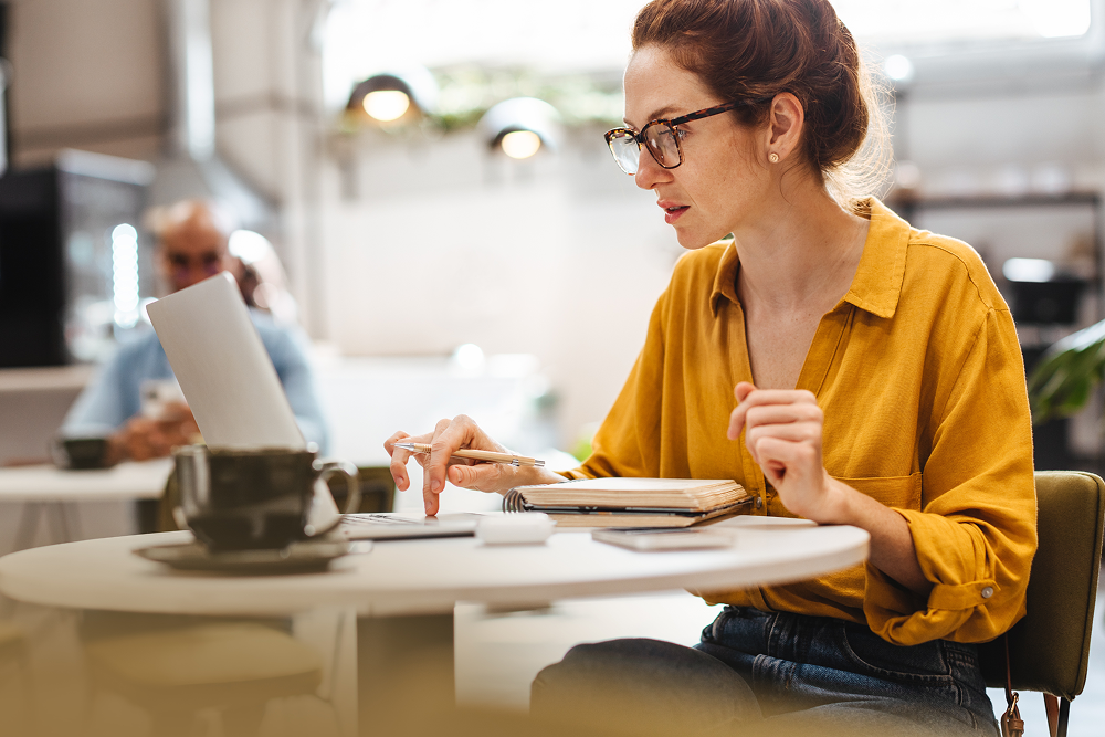 Mulher trabalhando no computador em uma cafeteria. Diferença entre graduação e pós-graduação