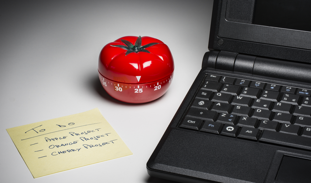 Timer em formato de tomate e computador para trabalhar usando o método pomodoro.